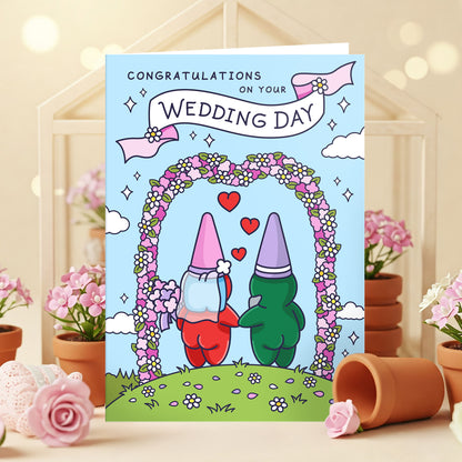 A lifestyle photoshoot of an illustrated wedding card showing a charming gnome couple ready to exchange vows under an archway of colourful flowers. The scene is romantic and full of character.
