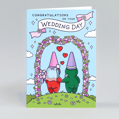 An illustrated wedding card showing a charming gnome couple ready to exchange vows under an archway of colourful flowers. The scene is romantic and full of character.