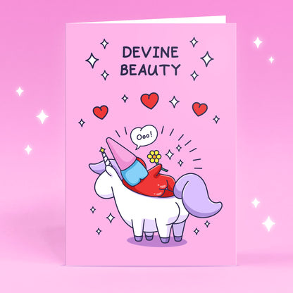 A cheeky lady gnome is laying on a unicorn with flowers, sparkles and hearts. This beautiful card has the caption 'Devine Beauty'.