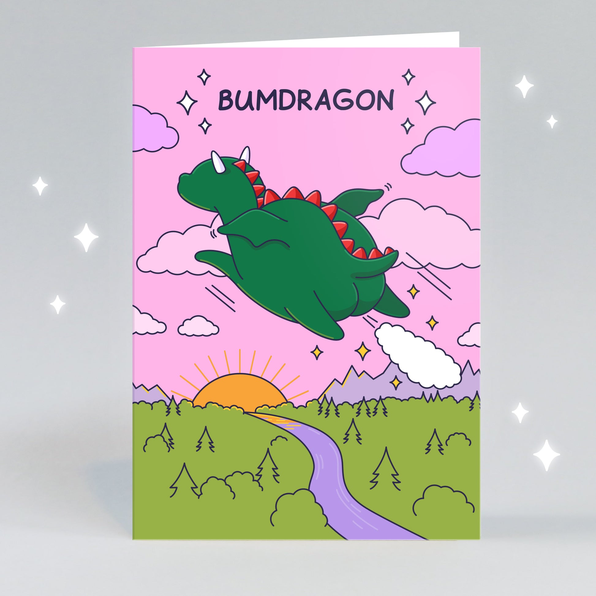 A funny greeting card of a dragon farting as he files over a beautiful sunset with a pink sky. The caption reads 'Bumdragon'.