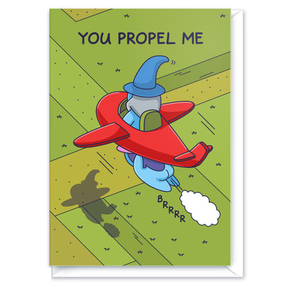 A greeting card of a Wizard sitting in a cute red plane with a Witch flying propelling him forward. The caption reads 'You Propel Me'.